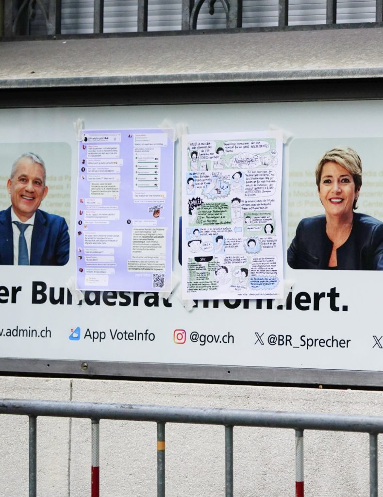 Infotafel beim Medienzentrum des Bundes, wobei die zwei Portraits der SVP-Bundesräte überklebt sind mit Anti-SVP-Plakaten